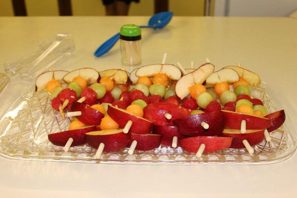 A tray of colorful fruit skewers made with apples, melon, grapes, and watermelon, served as healthy snacks for kids.
