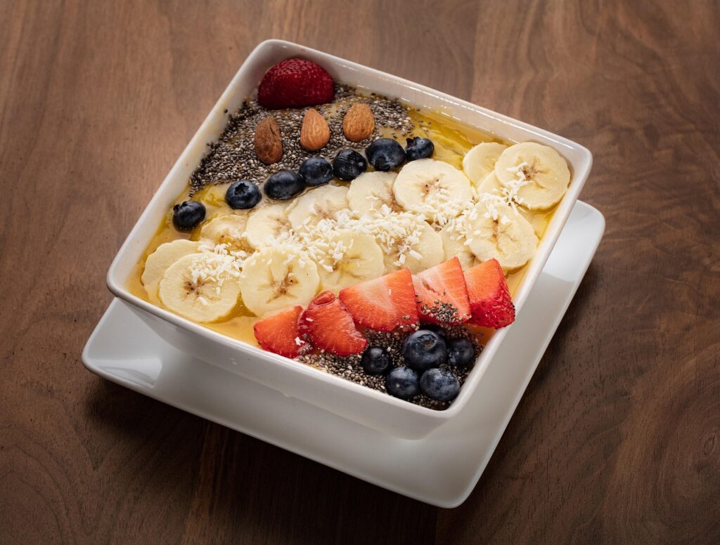 Colorful smoothie bowl topped with banana slices, strawberries, blueberries, chia seeds, almonds, and shredded coconut – healthy snacks for kids