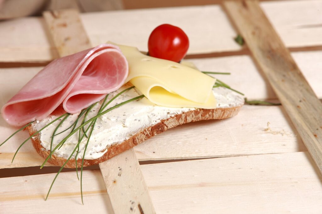 Open-faced sandwich with cream cheese, ham, cheese, chives, and a cherry tomato – healthy snacks for kids