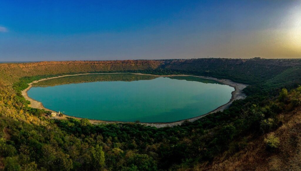 Aerial view of Lonar Lake in Maharashtra, a circular crater lake formed by a meteor impact, surrounded by forested rim and clear sky