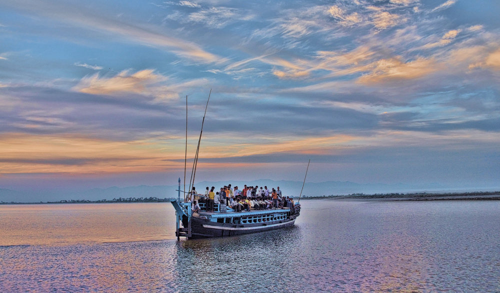 People on a boat crossing the Brahmaputra River during sunset on the way to Majuli Island, Assam