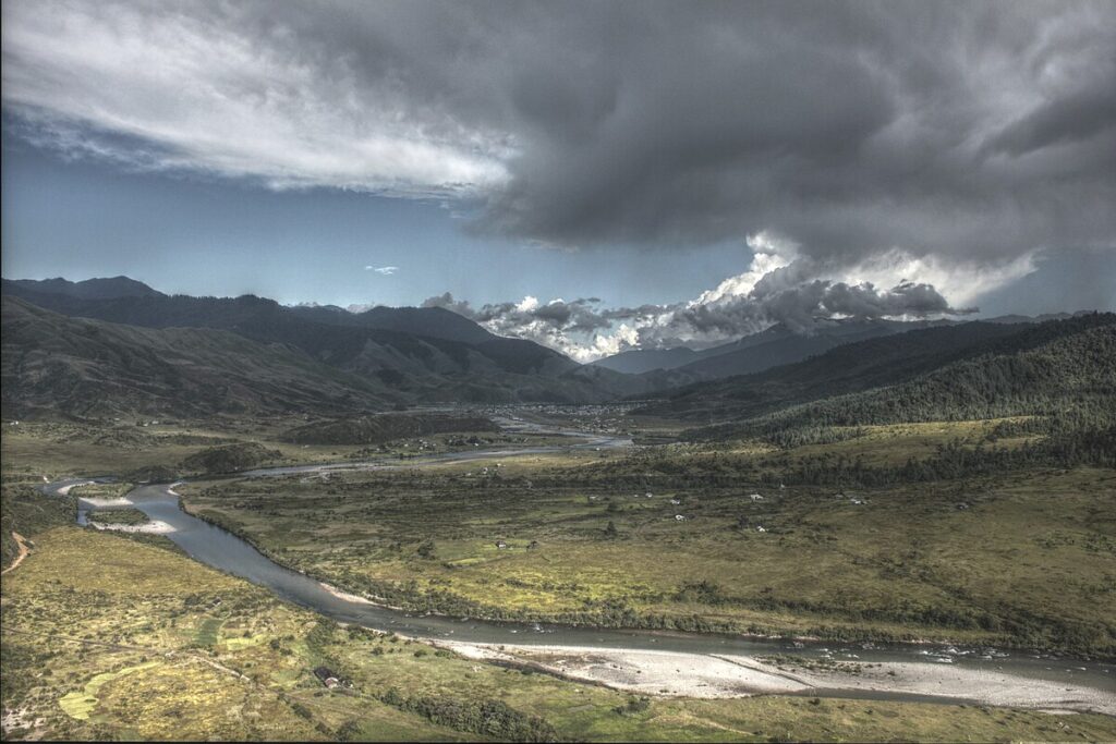 Aerial view of Mechuka Valley in Arunachal Pradesh with a winding river and surrounding mountain landscape under dramatic clouds