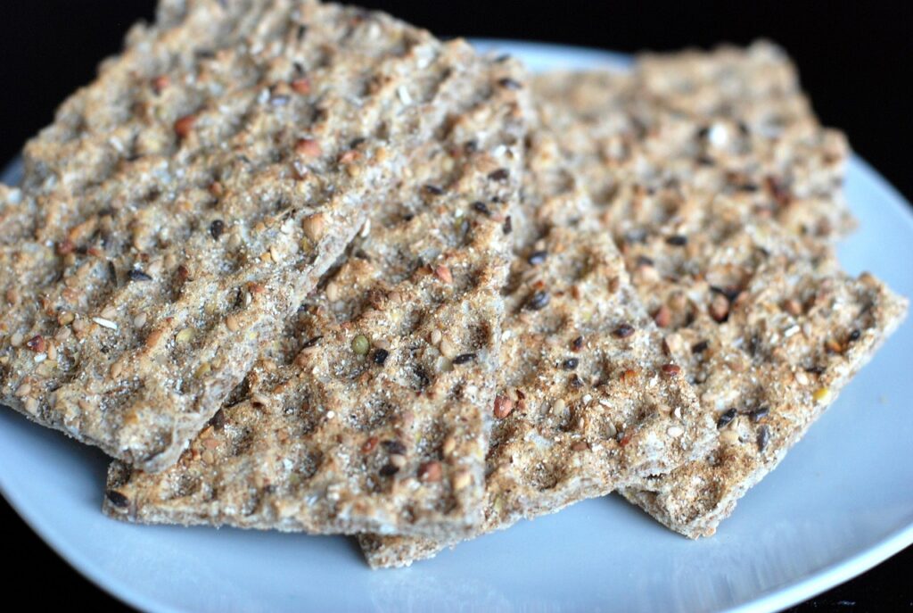 Close-up of whole grain crispbread with seeds on a white plate, served as a healthy snack for kids.