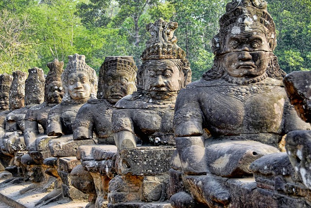 Ancient stone guardian statues at Angkor Thom in Cambodia, depicting mythological figures with intricate carvings and expressions, surrounded by lush greenery.