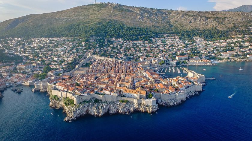 Aerial view of Dubrovnik, Croatia, showcasing its historic old town with terracotta rooftops, surrounded by ancient city walls and bordered by the deep blue Adriatic Sea, a romantic and budget-friendly honeymoon spot.