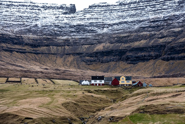 Most beautiful places in the world – scenic view of colorful houses in the remote Faroe Islands nestled beneath dramatic, snow-dusted cliffs.
