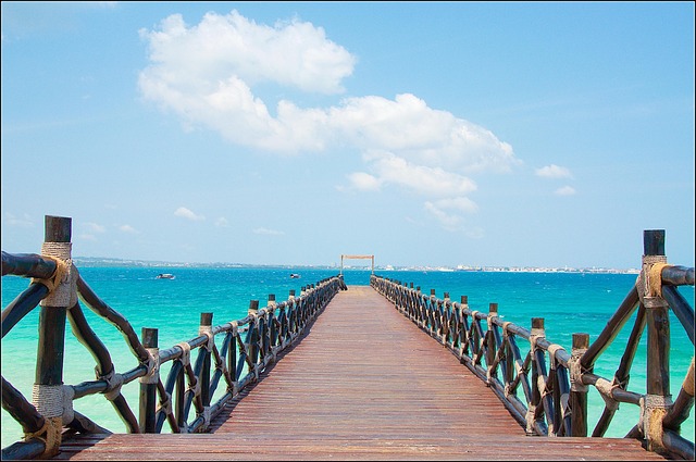 Wooden pier extending into the turquoise waters of Zanzibar, Tanzania, under a bright blue sky, offering a serene and romantic budget-friendly honeymoon escape.