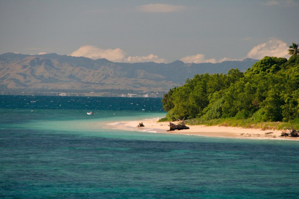 Fiji island view with palm-fringed beaches, turquoise waters, and traditional thatched huts creating a perfect tropical paradise scene.