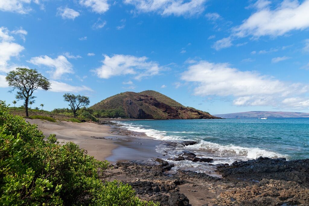 Scenic coastline of Maui, Hawaii with golden beaches, lush green mountains, and the Pacific Ocean under a clear sky.
