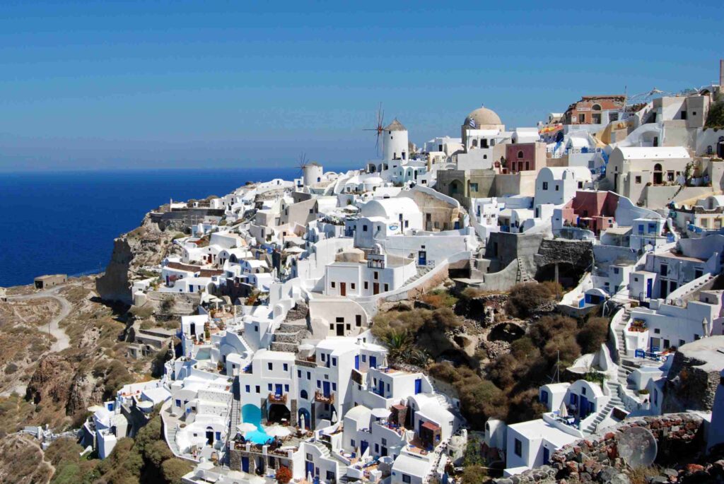Santorini, Greece with iconic whitewashed houses, blue-domed churches, and volcanic cliffs overlooking the Aegean Sea at sunset.
